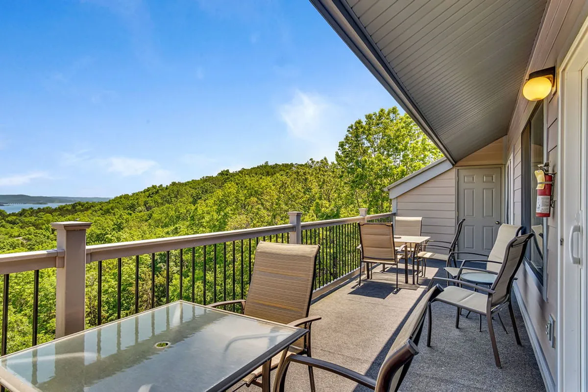 A scenic exterior view of an outdoor seating area with a glass-top table, lush greenery, and a distant view of hills and water. The setting feels peaceful and ideal for gatherings, morning coffee, or stargazing—activities that complement returning to the condo and unwinding together as a family.