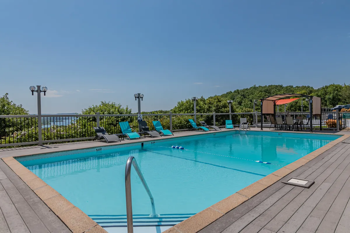 A vibrant outdoor scene featuring a large swimming pool surrounded by lounge chairs and lush landscaped greenery. The area includes a covered canopy seating area, ideal for group gatherings or relaxing with family and friends. The tranquil atmosphere suggests a resort-style experience.