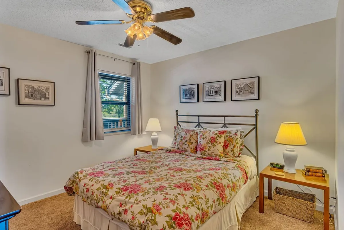 A cozy bedroom with a comfortable bed dressed in floral bedding, two bedside lamps, and framed pictures above the bed. The room radiates warmth and tranquility, perfect for guests or family members to unwind.