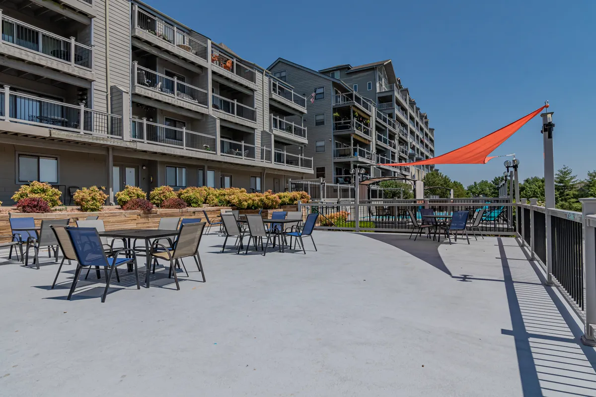 An inviting outdoor seating area adorned with colorful flowers under a shade sail offers a relaxing place to unwind. The setup hints at enjoying the lakeside atmosphere, with space for socializing and taking in sunset views.