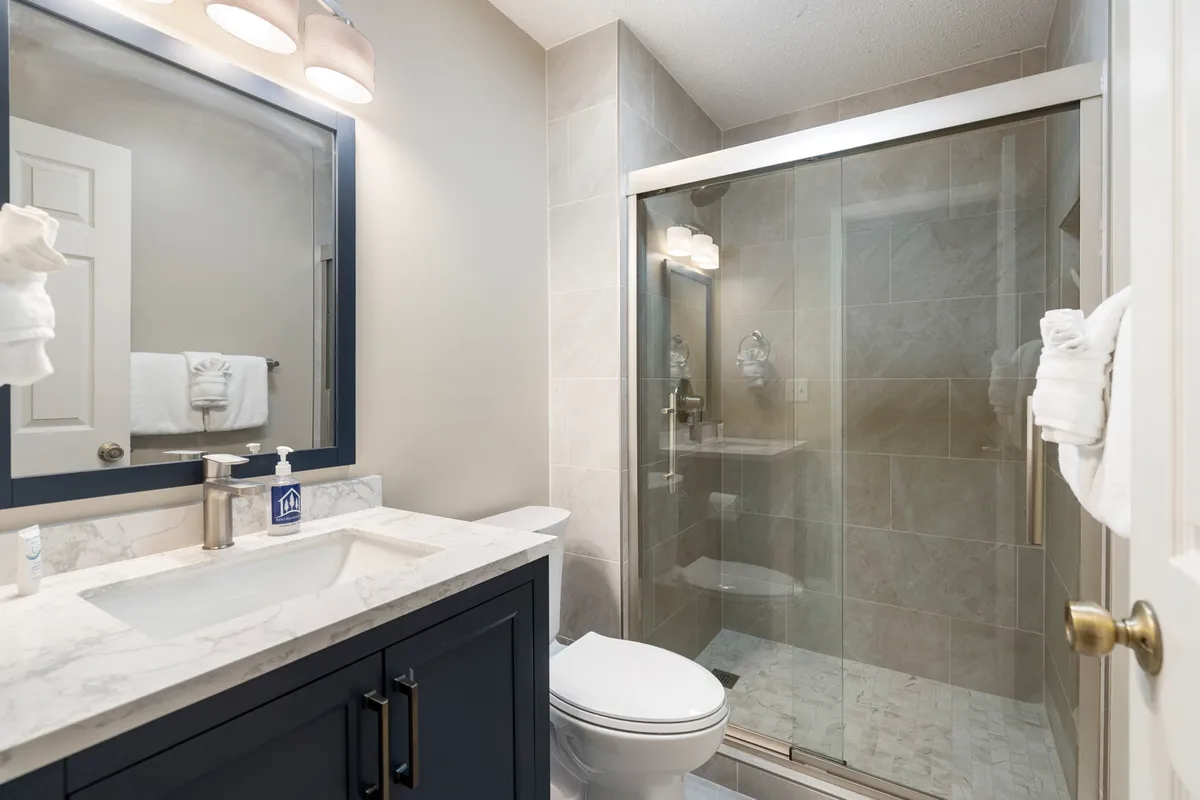 A modern bathroom with a marble countertop, glass shower enclosure, dark cabinetry, and a vanity mirror. The ambiance is serene and functional, ideal for refreshing after a day of fun.