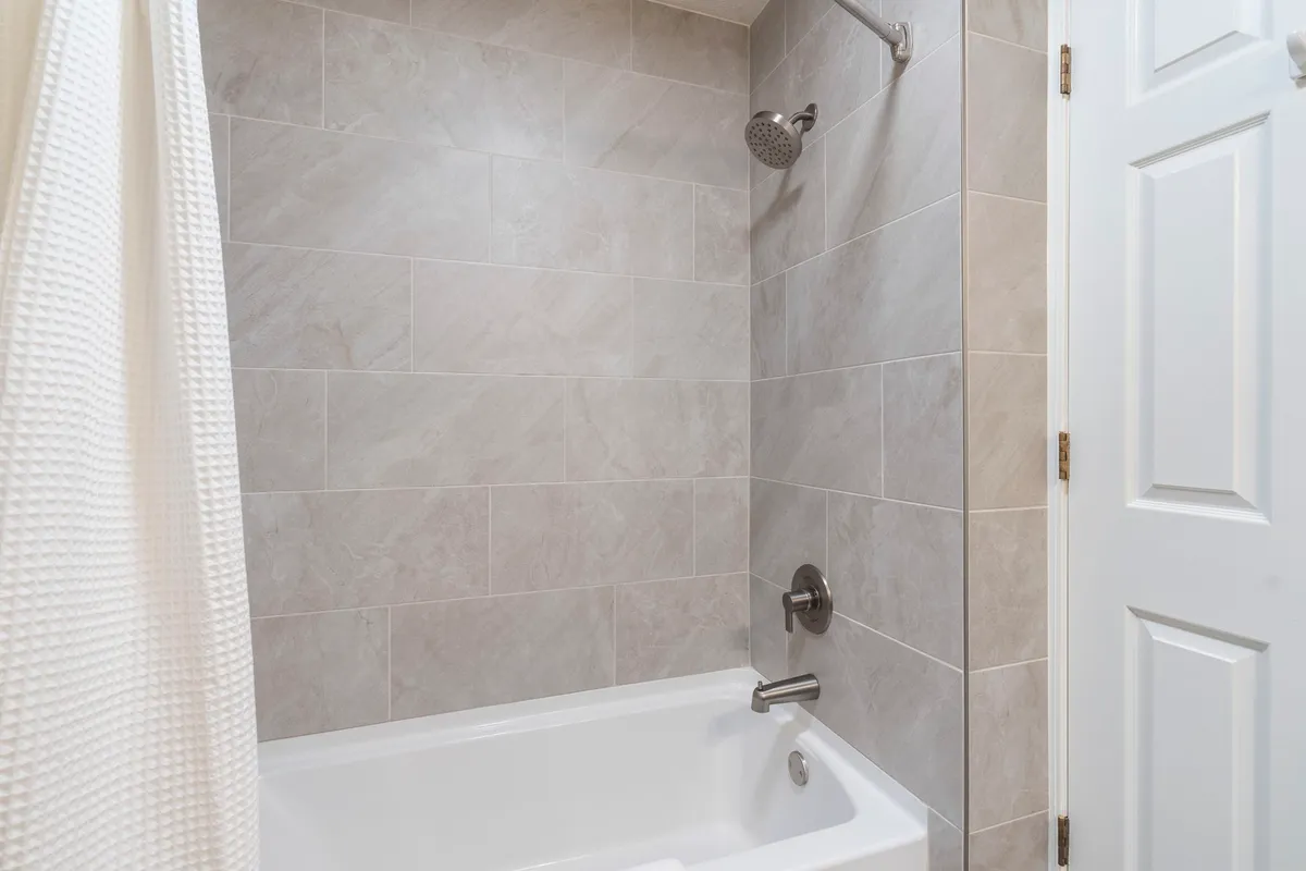 A fresh, modern bathroom with a bathtub, showerhead, and clean tiled walls. The space is designed for relaxation and rejuvenation, echoing the ensuite and guest bath amenities detailed in the section.