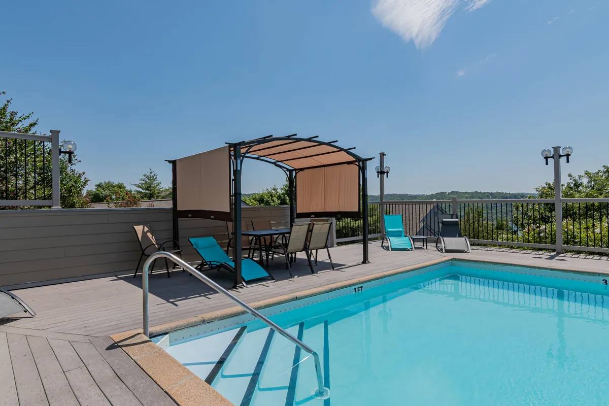 An inviting exterior shot of the resort's outdoor swimming pool area. The image features a canopy gazebo, poolside chairs, and a tranquil landscape view, suggesting relaxation and summertime fun with family after a day of adventure.