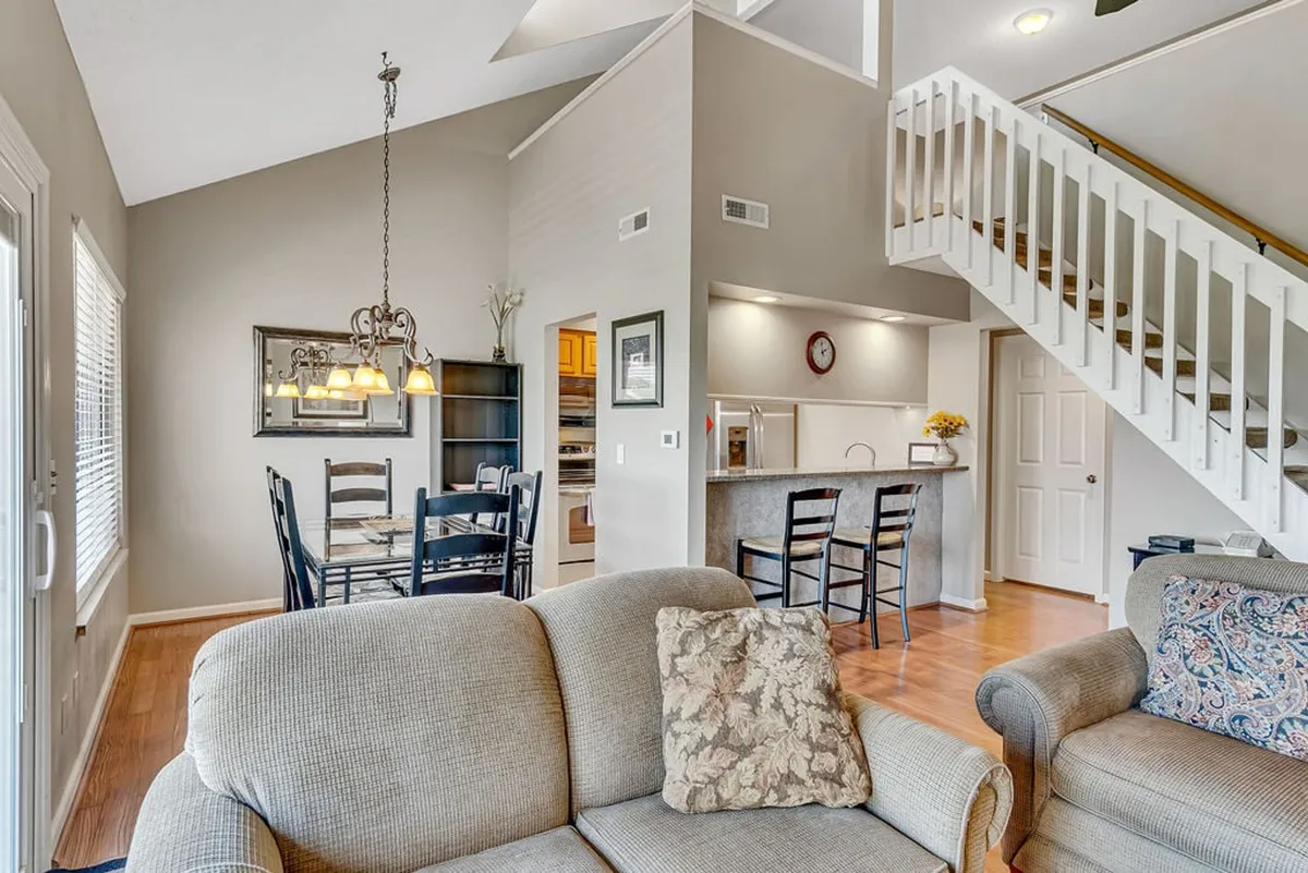 The hero image showcases a warm, inviting open-concept living area with a comfortable sofa, a family-friendly dining table, a stylish staircase, and a modern kitchen—perfect for relaxing, sharing meals, and making memories together.